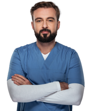 young bearded man wearing blue scrubs over a white long sleeved shirt while crossing his arms